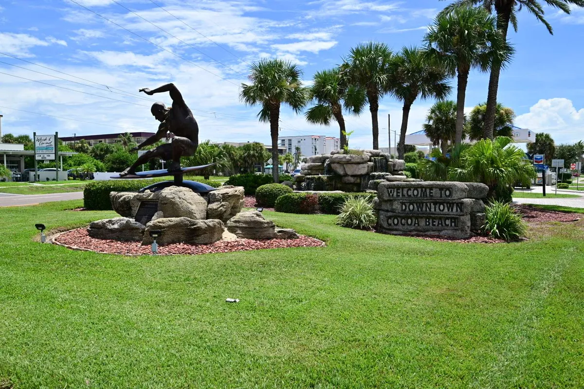 A surfer statue among palms and river-rock landscaping